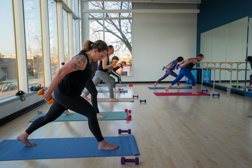 yoga sculpt participants lunge on mats with weights