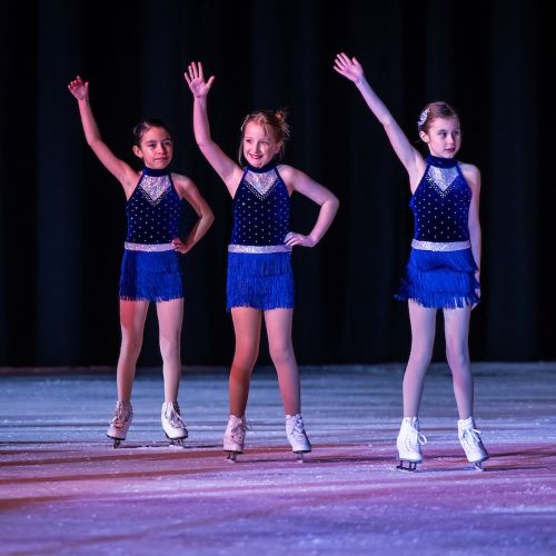 three skaters in blue costumes lift their arms during a routine