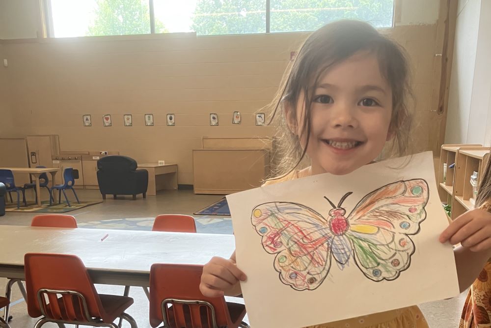 a young child holds up a picture of a butterfly colored in