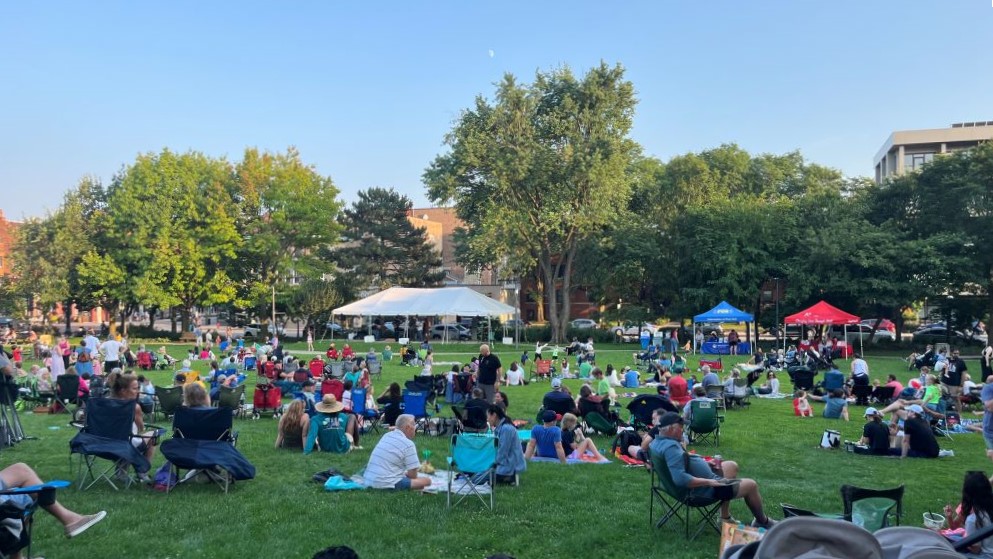 a large crowd sits on a grassy hill with sponsor tents in the background