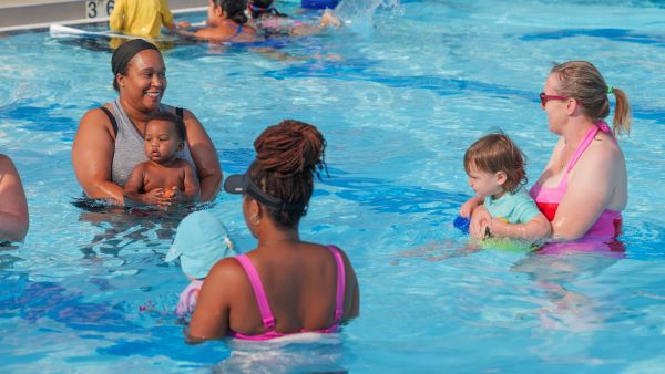 a group of moms and kids stand in the pool during a swim lesson