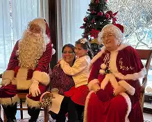 Santa Claus and Mrs. Claus pose with a mother and daughter in front of a decorated Christmas tree.