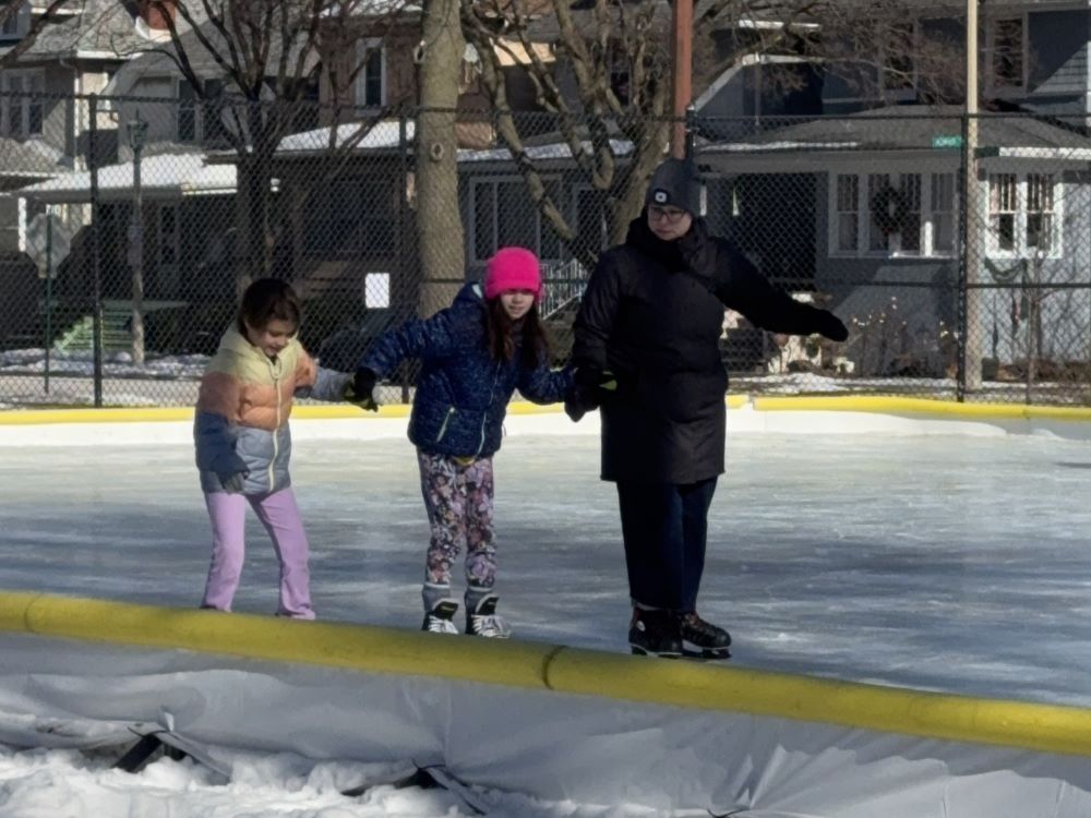 three people hold hands while skating on the outdoor rink