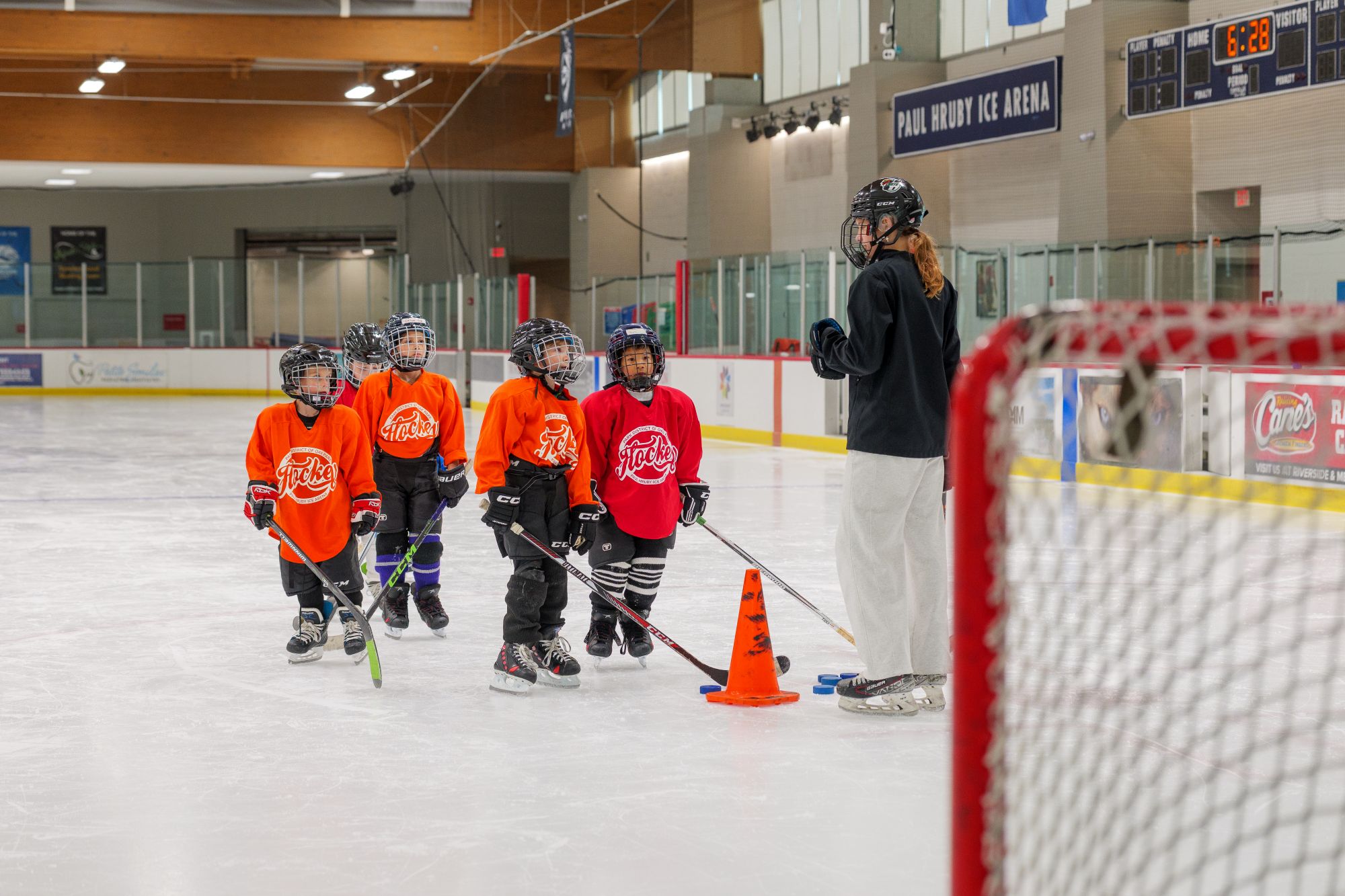 hockey students in red and orange jerseys listen to their coach